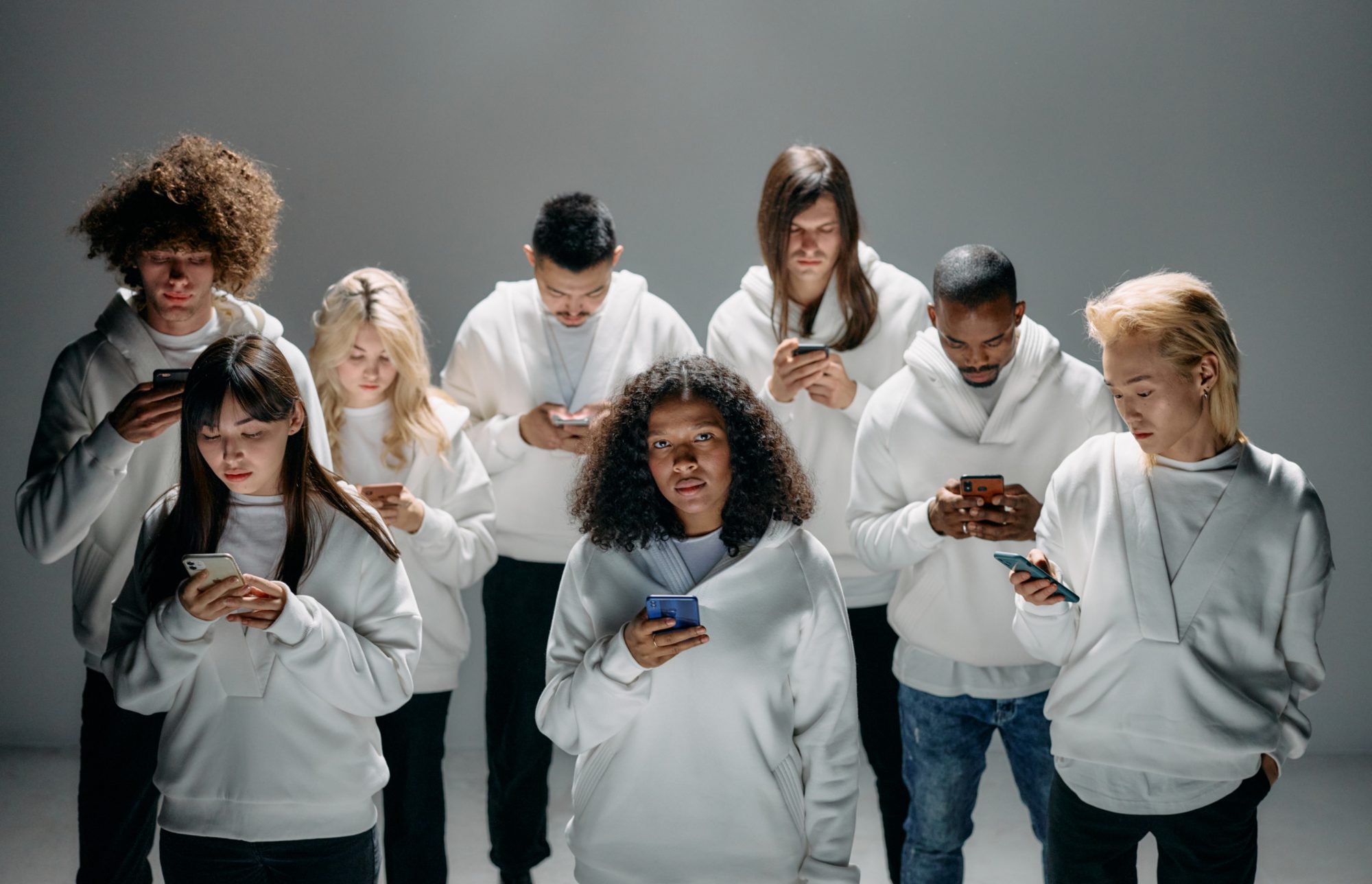 A group of young people in white hoodies, each absorbed in their phone